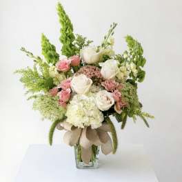 Pink and white roses arranged in a glass vase with green accents