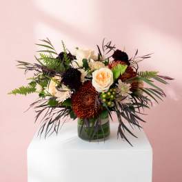 Mixed bouquet of cream, peach, and burgundy flowers in a glass vase