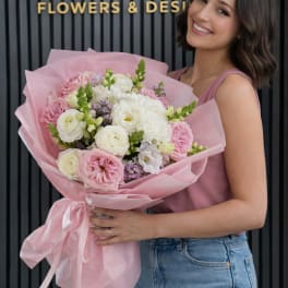 Woman holding a pink-wrapped bouquet of pink and white flowers