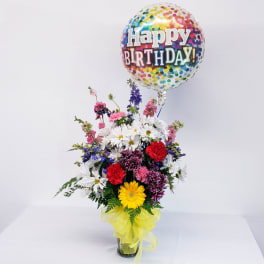 Birthday balloon above a mixed flower arrangement in a glass vase