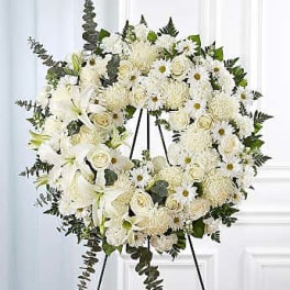 White funeral wreath on a black easel with lilies and roses