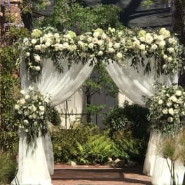 White floral wedding arch with draped fabric and greenery