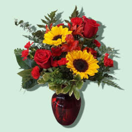 Bouquet of red roses and yellow sunflowers in a red glass vase