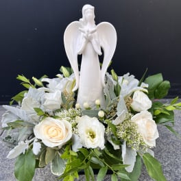White angel figurine surrounded by white roses and greenery