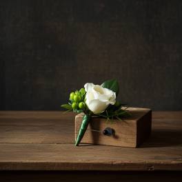 White rose boutonniere with green berries resting on a small wooden block