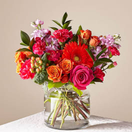 Mixed bouquet of pink, orange, and red flowers in a clear glass vase