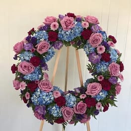 Circular floral wreath on a wooden easel with pink, blue, purple, and red blooms