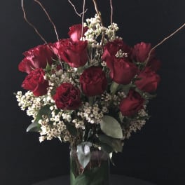 Red roses and white filler flowers in a tall glass vase with curly branches