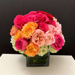 Bouquet of pink, peach, and orange roses in a square glass vase