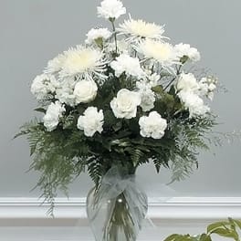 Tall arrangement of white roses, carnations, and spider mums in a clear glass vase with bow