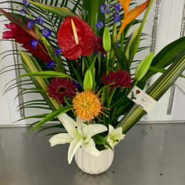 Tropical flower arrangement in a white vase with red, orange, purple, and white blooms