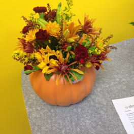 Autumn flower arrangement in a pumpkin container with yellow and burgundy blooms