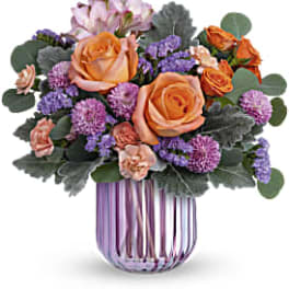Orange roses and purple flowers in a striped glass vase