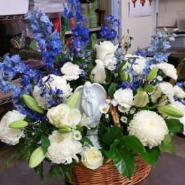 White and blue floral arrangement in a wicker basket with a small angel figurine
