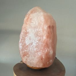 Pink salt lamp on a wooden base against a plain wall