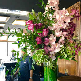 Tall floral arrangement with pink orchids and roses in a glass vase