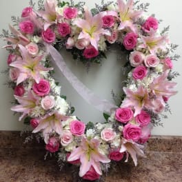 Heart-shaped wreath of pink roses and lilies with a white ribbon