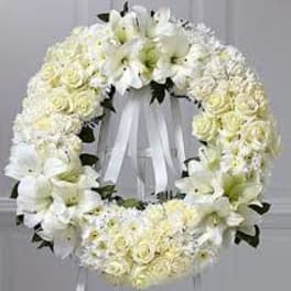 White floral funeral wreath with lilies and roses on a ribbon stand
