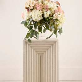Blush and white floral arrangement on a pedestal with trailing greenery