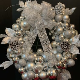 Silver decorative wreath with glittery ornaments and a large mesh bow