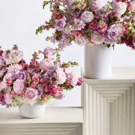 Two pink floral arrangements in white vases on textured pedestals