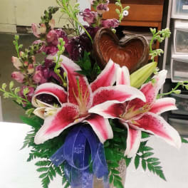 Pink stargazer lilies in a vase with a purple ribbon and heart-shaped accent