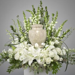 White floral arrangement with lilies and roses around a stone urn