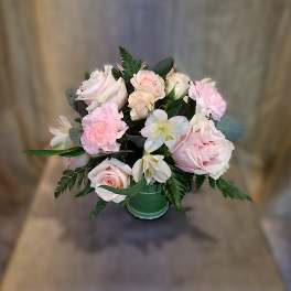 Compact arrangement of pale pink roses, carnations, and white alstroemeria in a green glass vase
