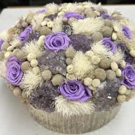 Purple roses arranged with dried beige accents in a round box