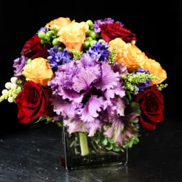 Bouquet of red, orange, and purple flowers in a square glass vase