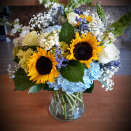 Sunflowers, blue hydrangeas, and white roses in a glass vase