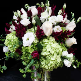White roses and green hydrangeas in a silver vase with burgundy accents