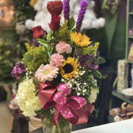 Mixed bouquet in a glass vase with roses, sunflowers, and a pink ribbon