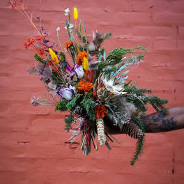Wildflower bouquet with dried blooms and pinecones held against a pink brick wall