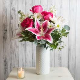 Pink roses and a stargazer lily in a white vase with a lit candle nearby