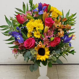Colorful mixed bouquet in a white pedestal vase with roses, sunflowers, and irises