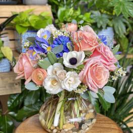 Mixed bouquet of pink roses, white anemones, and blue flowers in a glass vase