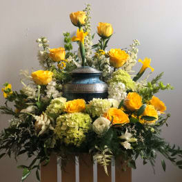 Yellow roses and white flowers arranged around a blue urn