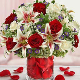 Bouquet of red roses and white lilies in a glass vase with rose petals