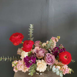 Mixed bouquet of roses, ranunculus, and pink blooms in a low vase
