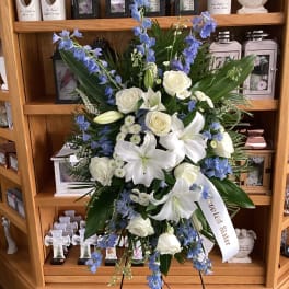 Standing sympathy spray with white lilies, roses, and blue flowers on an easel