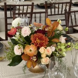 Mixed floral centerpiece in a low gold vase on a banquet table