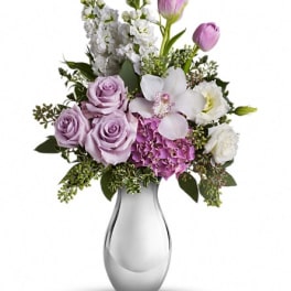 Lavender roses and white orchids arranged in a glass vase