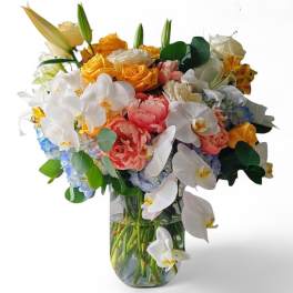 Mixed bouquet of white orchids, roses, lilies, and hydrangeas in a glass vase