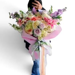 Large pastel bouquet of roses, lilies, and orchids wrapped in pink paper