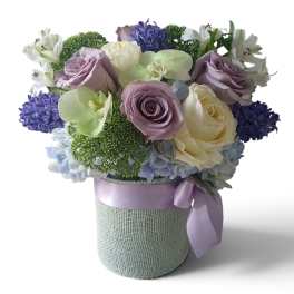 Lavender roses, white blooms, and blue flowers in a wrapped hatbox arrangement
