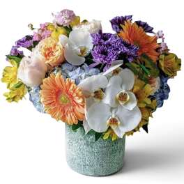 Mixed bouquet with orchids, gerbera daisies, roses, and hydrangeas in a textured vase