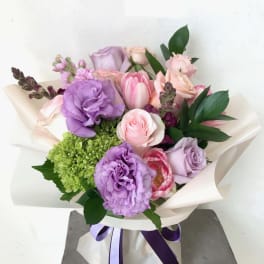 Bouquet of pink and lavender flowers wrapped in white paper with a purple ribbon