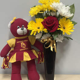 Bouquet of yellow and white daisies with a red rose in a black vase beside a teddy bear