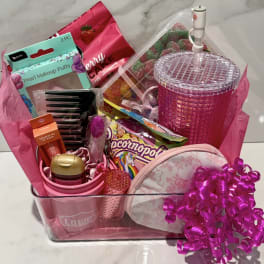 Pink gift basket with candy, makeup items, and a glittery tumbler